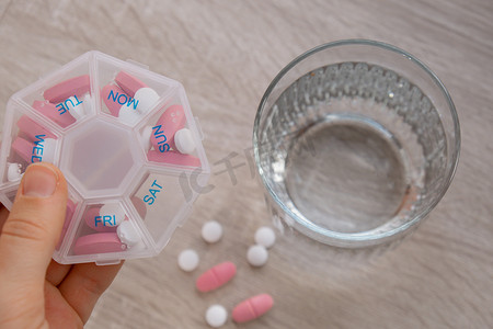 妇女分拣药丸组织者每周拍摄药丸盒特写镜头，每天服用药片剂量，用白色粉红色药物和胶囊服药。