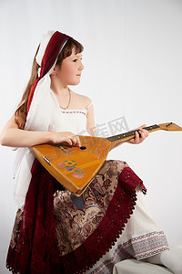 在工作室的白色背景上，身着程式化的鞑靼民族服装、乐器巴拉莱卡的小女孩的画像。