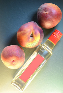 三个成熟的桃子特写在一个瓶子上，瓶子上有一个粉红色的标签，在浮雕皮革般的天蓝色绿色背景上，顶视图