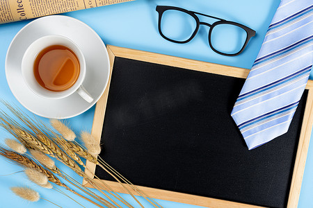 快乐父亲节背景概念与蓝色领带眼镜、报纸、干草花、一杯茶和蓝色背景的黑板，带有文本复制空间。