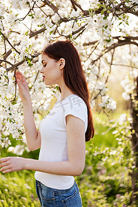 一位身穿休闲服、头发红的快乐女人的画像，抚摸着果树枝上的花朵