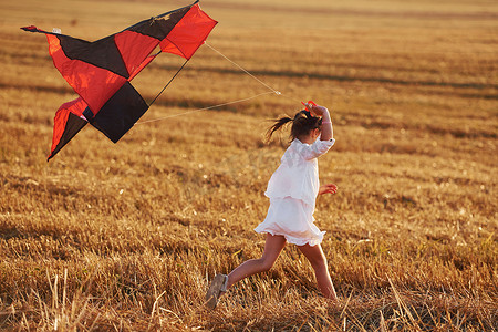 夏天，快乐的小女孩在田野里带着红风筝在户外奔跑