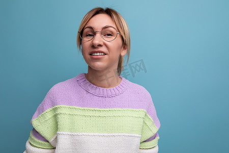 一位身穿条纹毛衣、戴着眼镜的可爱金发女性的特写照片，蓝色背景上有复制空间