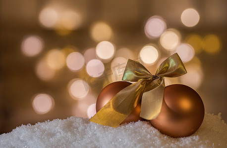 个蝴蝶结摄影照片_圣诞装饰，雪上有两个带蝴蝶结的金球，闪闪发光的背景