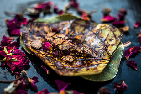 黑色表面上著名的印度传统马萨拉锅或 meetha 锅的特写，上面有一些玫瑰水，包括涂有 sauf、supari、甜味剂和一些椰子粉。