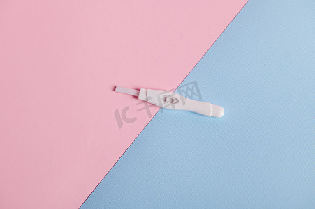 粉色和蓝色柔和双色背景上阳性妊娠试验套件的孤立平面照片。