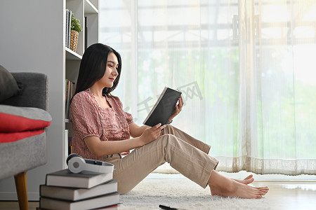 美女坐在客厅地板上看书，在家度过休闲周末