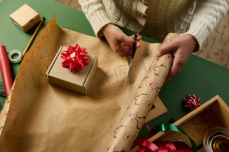 女性在为圣诞节、新年或任何其他庆祝活动包装礼物时切割包装纸的俯视图
