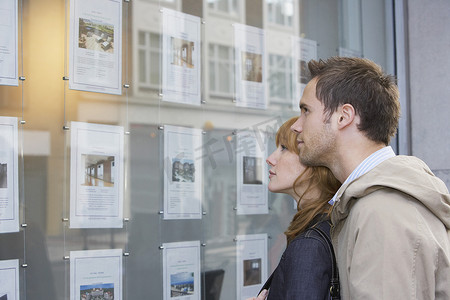 橱窗广告摄影照片_一对年轻夫妇在房地产办公室看橱窗的侧视图