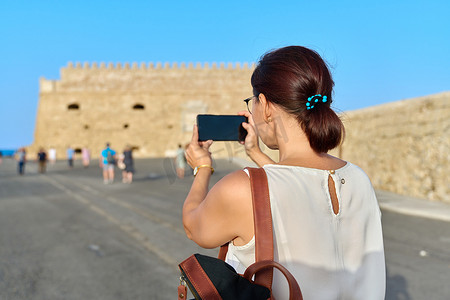 女游客在智能手机上拍照，这是一座古老的海滨堡垒