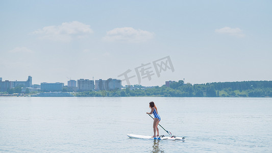 穿泳衣女孩摄影照片_身穿条纹泳衣的白人女性骑在 SUP 板上。