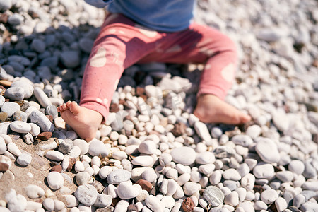 穿着红裤子的小孩坐在卵石滩上。