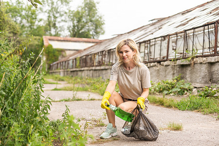 戴乳胶手套的女人把垃圾捡到垃圾袋，手里拿着用过的塑料瓶，照顾地球