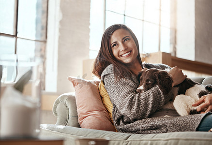 满足幸福摄影照片_女人在沙发上和狗一起放松，在家里和宠物一起微笑和满足，在客厅里与和平一起快乐。