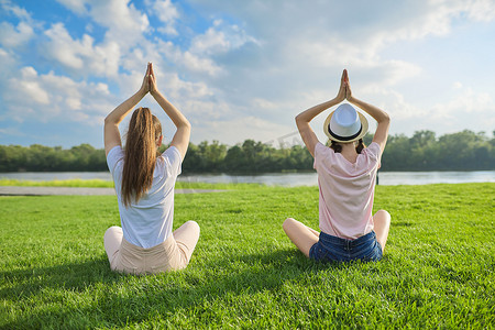 荷花绿背景摄影照片_两个女孩坐在绿草上的莲花位置，后视