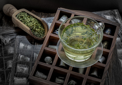 凉茶设计摄影照片_一杯热麻茶（CBD 凉茶）和干有机麻叶放在旧木箱上的复古顶针系列上。
