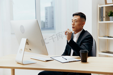 穿着西装的商人坐在电脑前的桌子旁喝着咖啡