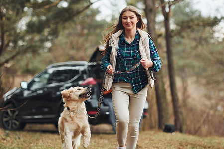 秋季或春季，快乐的女孩和她的狗在森林里散步