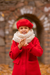 红色大气摄影照片_穿着红色外套和贝雷帽的白人女孩在秋天的公园散步时冻僵了。