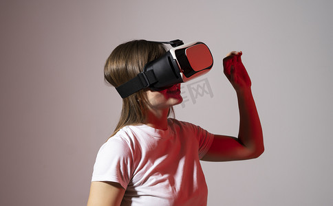 身穿白色 T 恤的女玩家戴着虚拟现实耳机，与朋友玩电子游戏，双手在红灯下打手势。