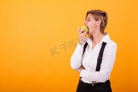 大口摄影照片_穿着便服的漂亮女人在黄色背景下咬了一大口青苹果。