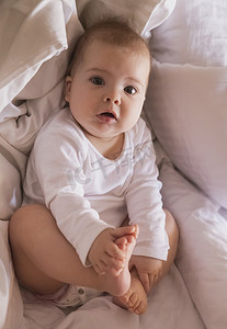 宝宝的腿摄影照片_可爱的宝宝躺在床上抱着他的腿