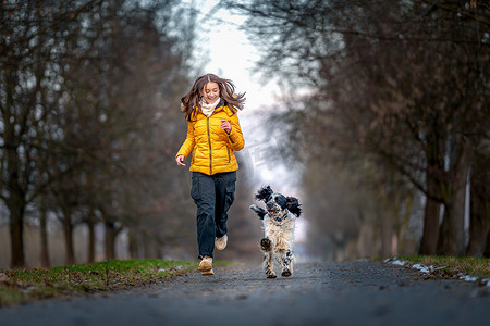 一个快乐的少年带着一只狗沿着树林间的小巷奔跑。