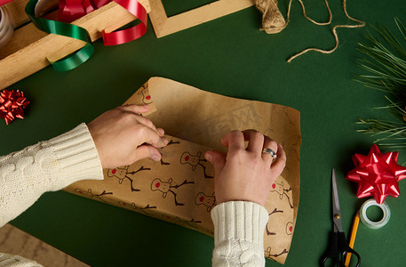 女人的手在绿色背景下为圣诞节或新年活动包裹礼物的顶部视图。