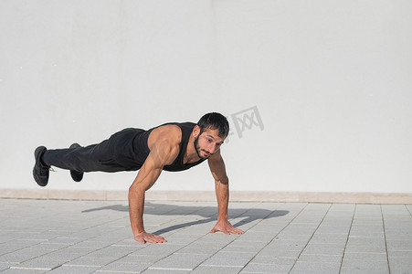 一名身穿黑色运动服的男子在户外做俯卧撑时跳跃。