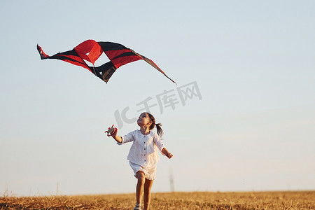 夏天，快乐的小女孩在田野里带着红风筝在户外奔跑