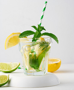 透明玻璃杯中的柠檬水，白色背景上有柠檬、酸橙、迷迭香小枝和薄荷叶