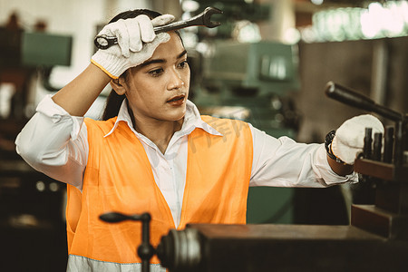 疲惫的亚洲女工在炎热的工厂里辛勤工作，用金属机器擦去汗水。