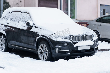 一辆宝马品牌的黑色轿车被白雪覆盖。