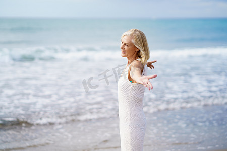 成熟的女人在沙滩上张开双臂，度过闲暇时光，享受闲暇时光