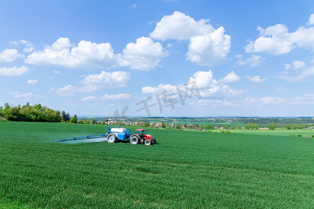 在拖拉机的帮助下，农村地区的小麦被喷洒肥料或除草剂。