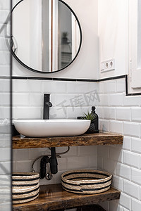 白色砖墙的浴室，木纹大理石台面上的椭圆形洗手盆，黑框墙上的圆形镜子映照着门口。