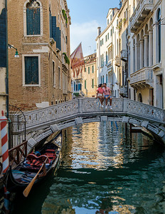 男女平等漫画摄影照片_一对男女在意大利威尼斯的城市旅行中坐在威尼斯运河上方的一座桥上