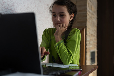 戴着耳机微笑的白人小女孩使用笔记本电脑与老师进行远程课堂视频通话，快乐的小孩与导师挥手致意，在电脑上在线学习，在家上学的概念