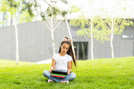 坐在草地上玩平板电脑的小女孩