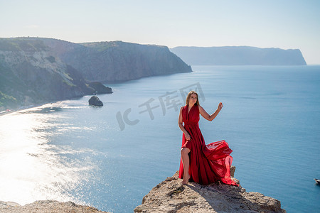 飘动摄影照片_在大海的映衬下，一位身着红色飞裙的女子在风中飘扬。