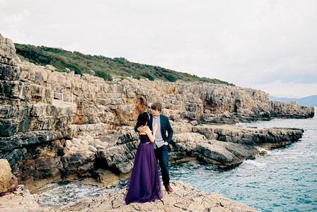 男人站在海边的石崖上，搂着女人的肩膀