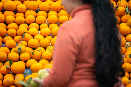 橘子 kinnu 柑橘类水果堆放在路边摊位上，展示农民传统上如何出售这种当地水果，而焦点不在的女人却在购买