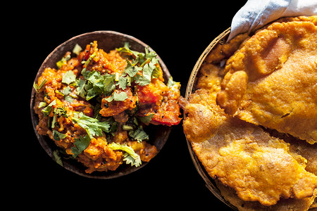 Batate ki sukhi bhaji 或土豆 sabji 在粘土碗中的特写镜头，以及一些干燥的普通油炸 puri 和一些黑色表面上的切洋葱。