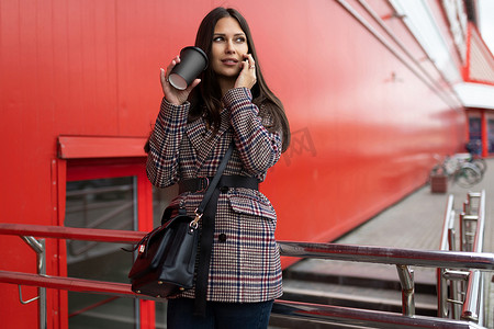 年轻女设计师在休息时在一栋红色建筑的背景下打电话