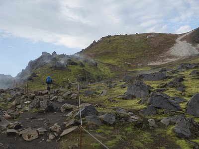 背着蓝色背包的徒步旅行者在多彩的 Rhyolit 彩虹山徒步旅行，那里有五颜六色的火山和地热喷气孔。