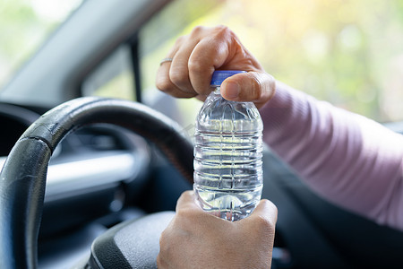 亚洲女司机开车时拿着瓶子喝水。