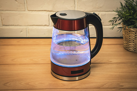 红色茶摄影照片_带起泡水的红色现代沸腾玻璃电热水壶特写