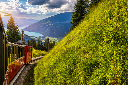 旅游列车摄影照片_红色旅游列车从因特拉肯附近的维尔德斯维尔开往瑞士著名的施尼格普拉特野花花园。