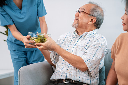 健康护士医生摄影照片_一位女护士为一对心满意足的老年夫妇端上一碗沙拉。