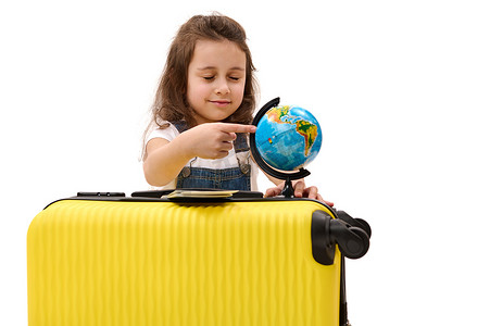 带手的地球摄影照片_5-6 岁快乐的欧洲小女孩带着手提箱，用手指指着地球，在白色背景中与世隔绝
